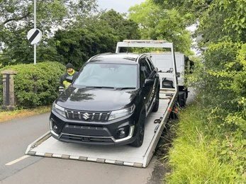 Black Suzuki being winched onto a flatbed recovery truck at the roadside